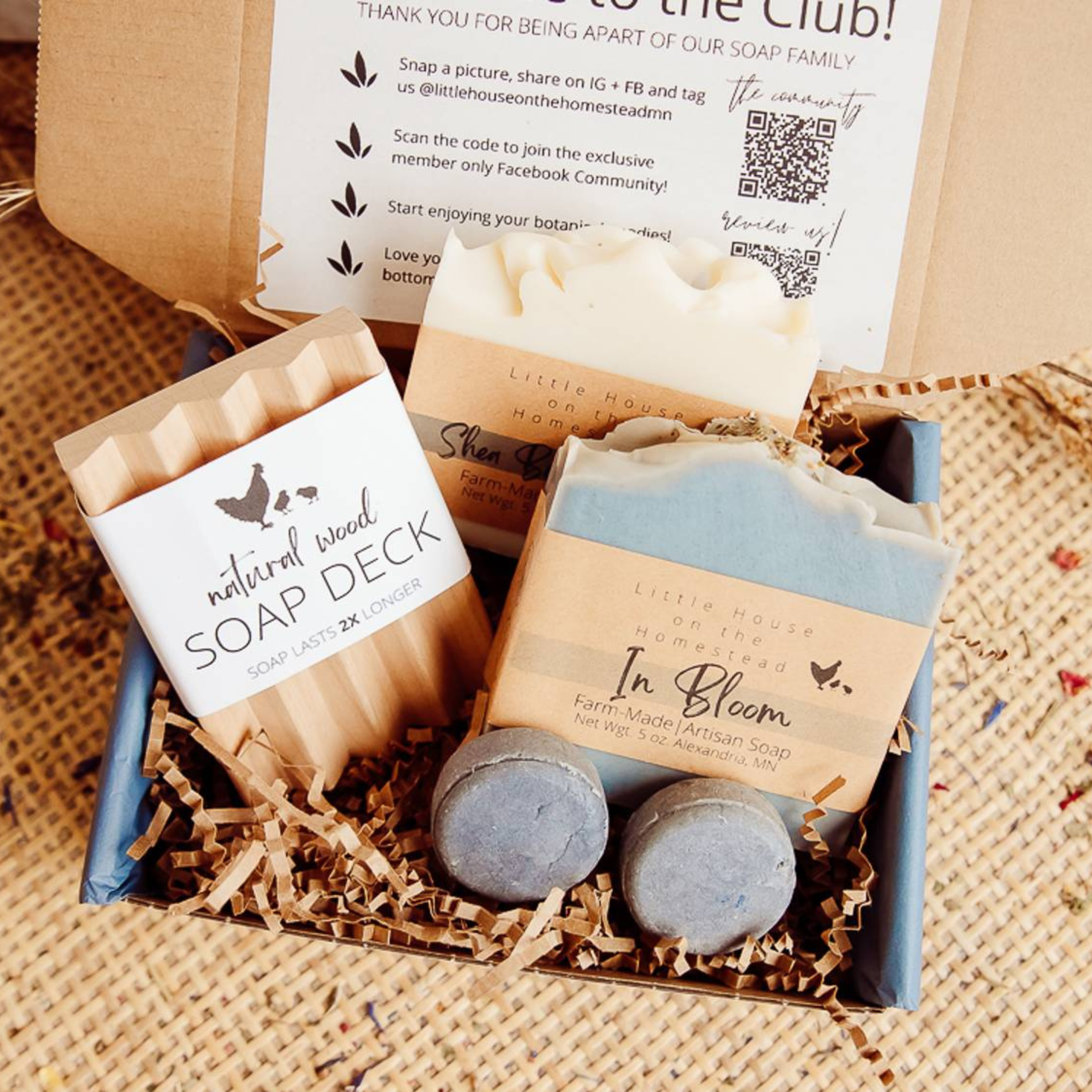 Two botanical handmade soaps, a 2 pack of tallow lip butters, in a kraft brown with cream colored tissue and shreds laying on a plaid fall colored shirt with yellow maple leaves on the ground.
