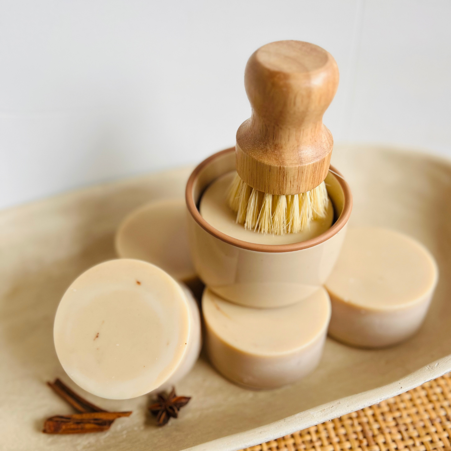 A set of handmade fall inspired dish soap bars and a wooden-handled soap brush arranged on a ceramic tray with star anise & cinnamon sticks.