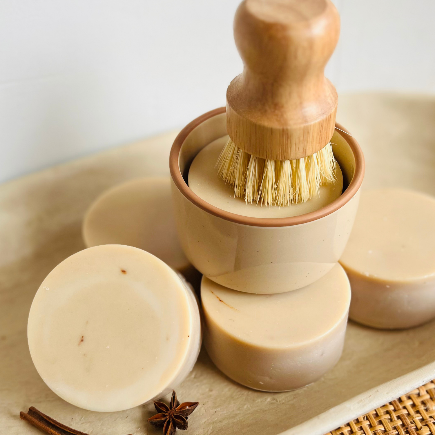 Cinnamon and frankincense scented dish soap bar showing natural cocoa-tinted color. Eco-friendly brush on top of a dish soap bar in a neutral colored ramekin. 